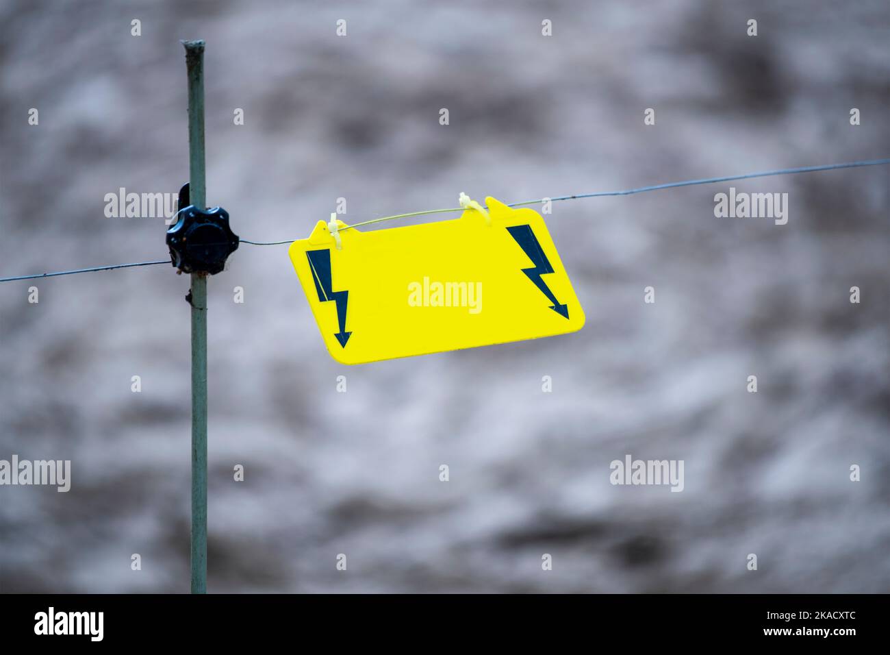 Electric fence warning sign. A yellow warning sign hangs on a wire and