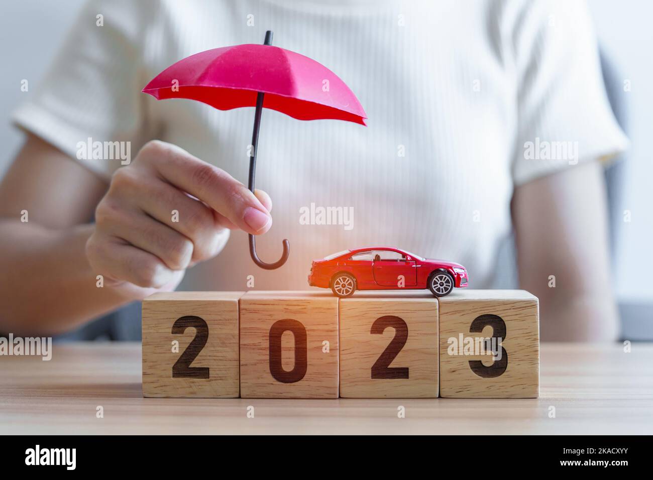hand holding umbrella and cover red car toy with 2023 Year block on table. Car insurance, warranty, repair, Financial, banking, money and New Year con Stock Photo