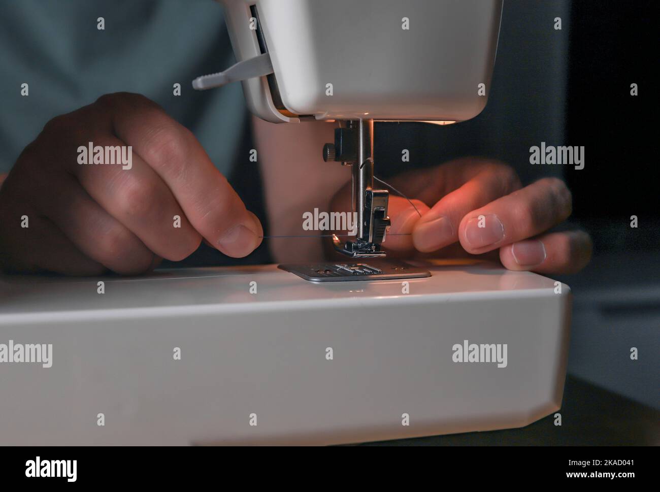 Male hands inserting thread through needle hole in sewing machine