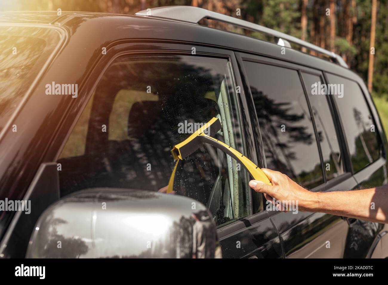 Driver hand with car cleaner cleaning and washing auto window in summer. Stock Photo