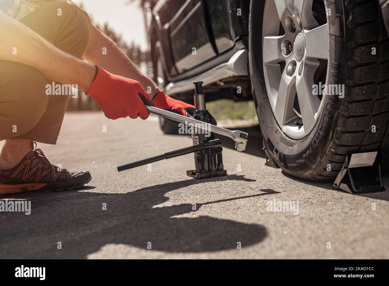 Hydraulic car jack is put under auto by hands in gloves, closeup. Stock Photo
