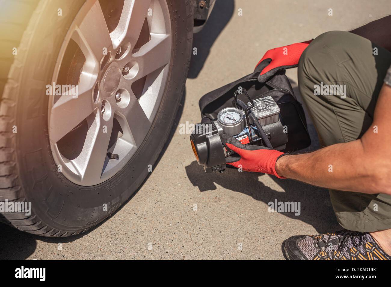 Male hands in glove and portable tire pump for inflating auto wheel. Tyre inflator air compressor with pressure gauge. Stock Photo