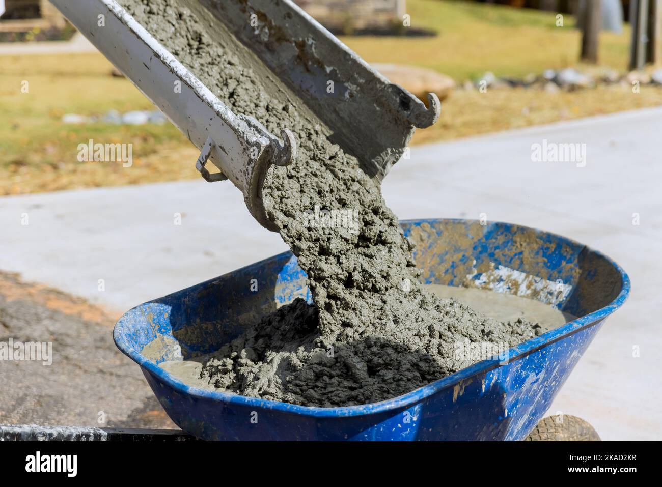 Concrete mixer truck pouring wet cement into blue wheelbarrow in