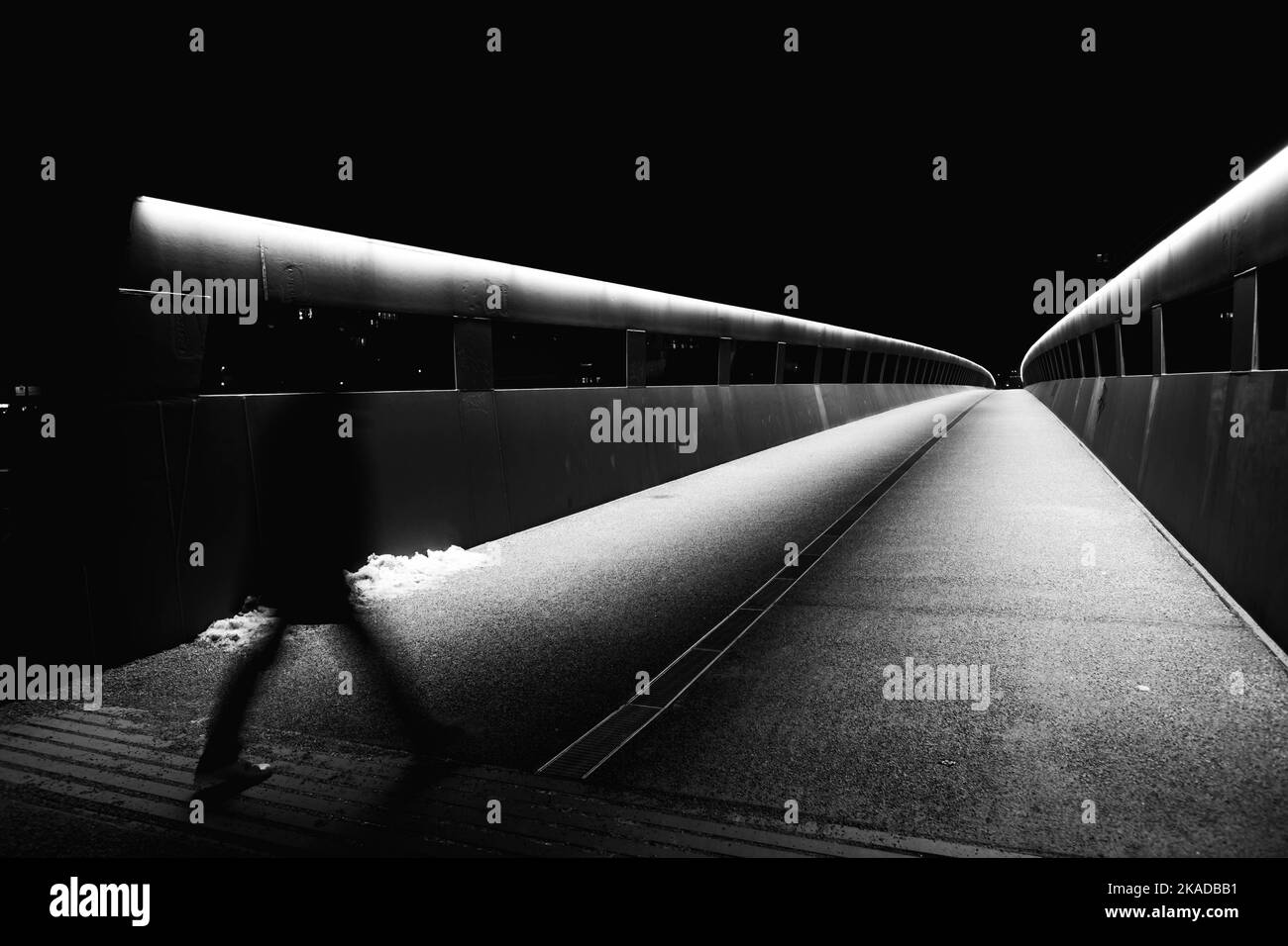 A grayscale shot of the person walking along the bridge at night. Stock Photo