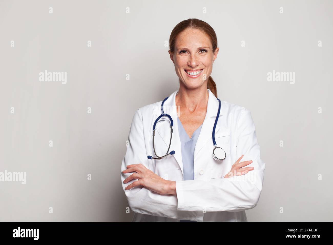 Attractive smiling female doctor in lab coat with arms crossed against