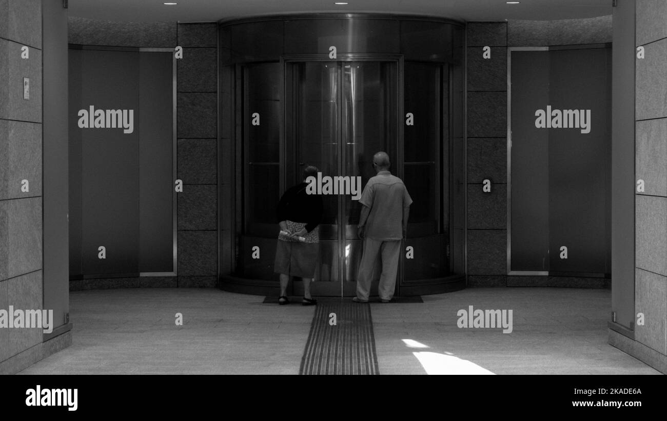 A grayscale shot of a couple of elderly by the glass doors of Gabriere station Stock Photo