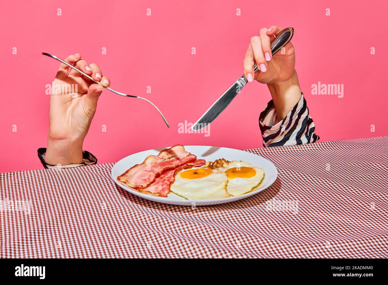 Female hands with fork and knife eating English breakfast with fried eggs and bacon Stock Photo