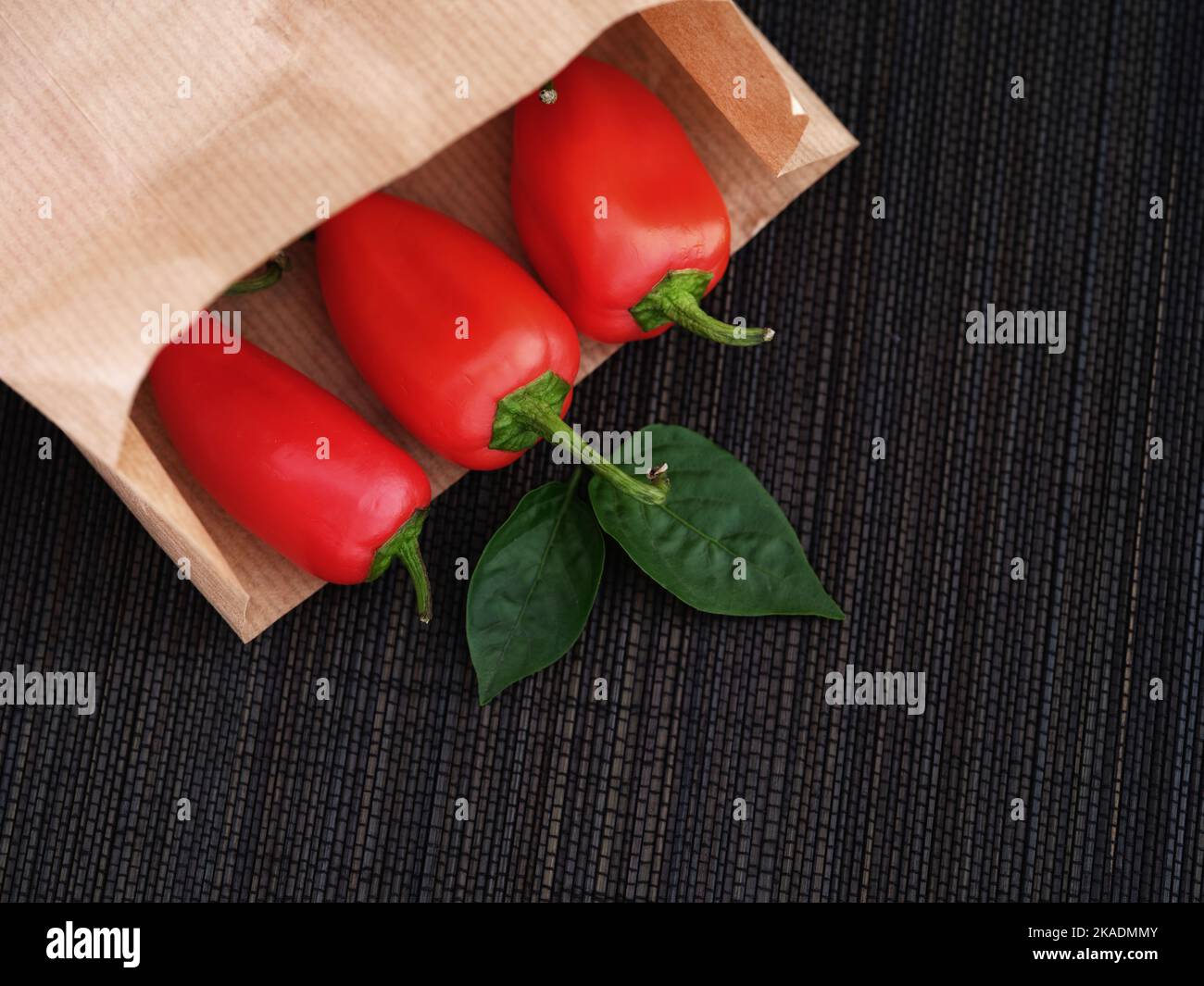 Some red bell peppers lying in a paper bag with some leaves near it. Close up. Stock Photo