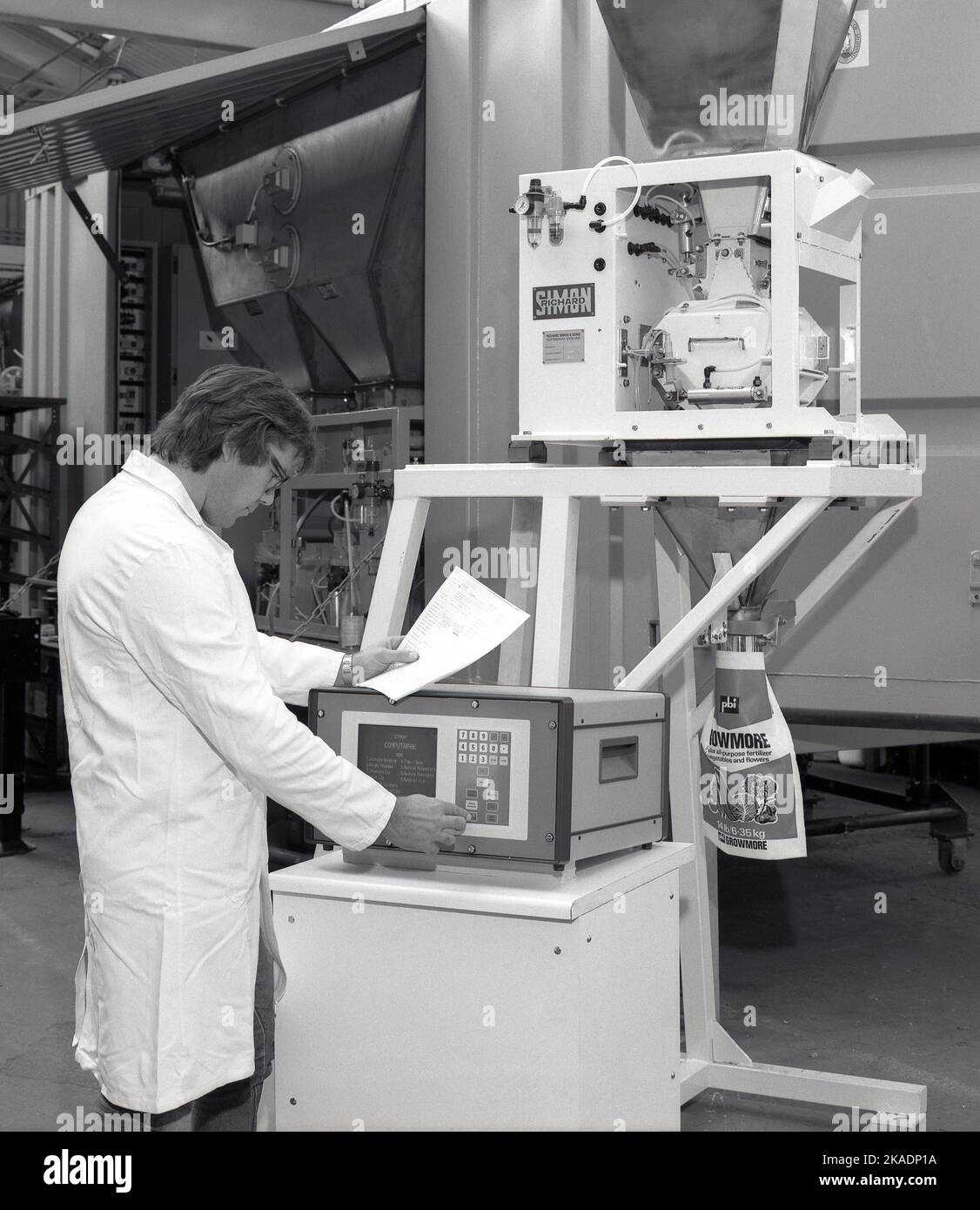 1980s, historical, male technican operating a machine's computer on a fertilser filling machine, made by Richard Simon & Sons, of Nottingham, England, UK. screen on machine says Simon Computapak, with menu giving options including weight Stock Photo
