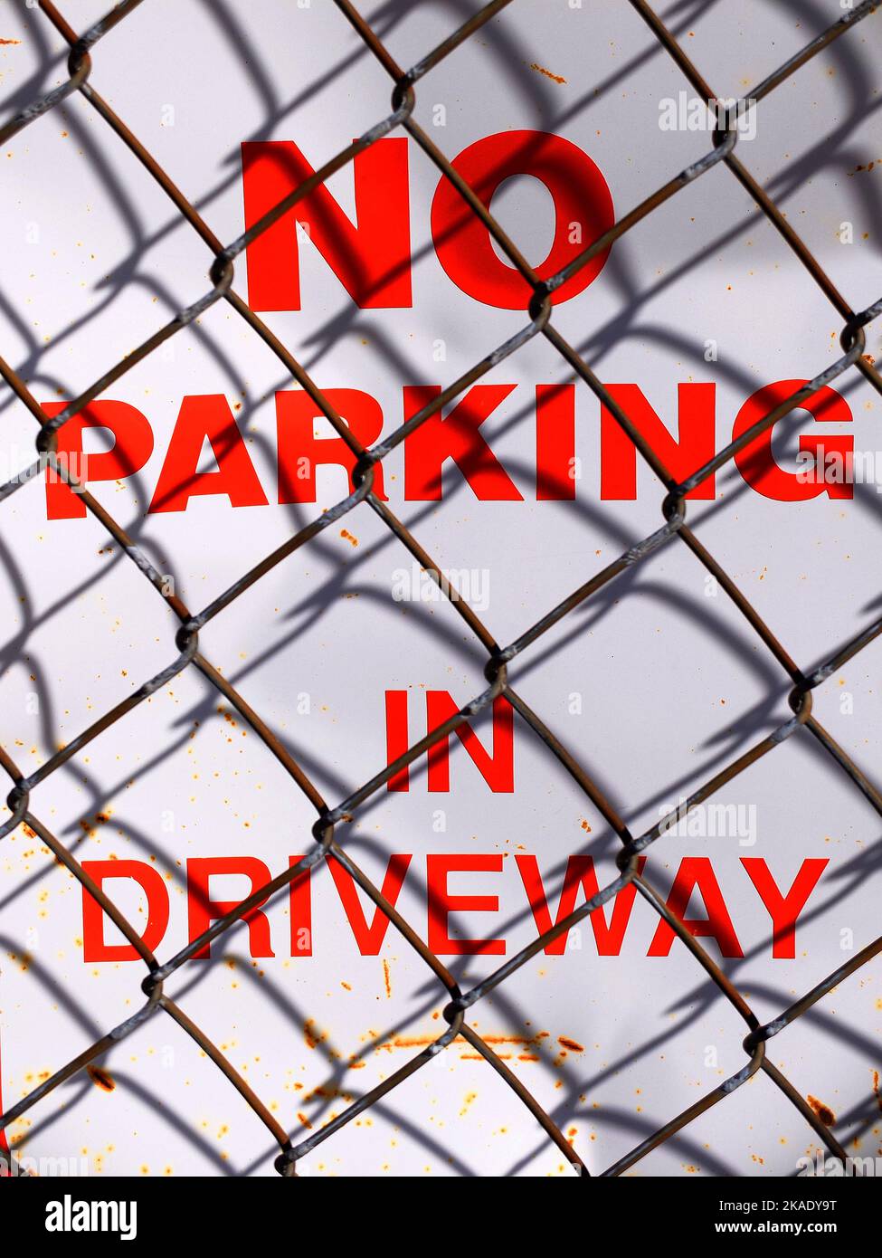 No parking in driveway sign with chain link chainlink fence shadows Stock Photo