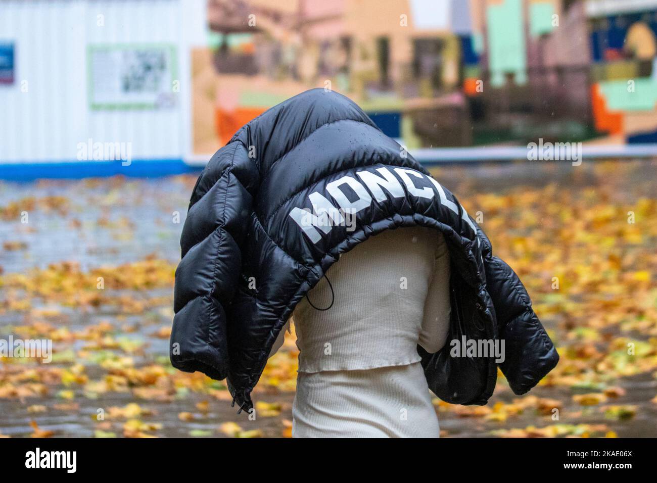 Woman holding Moncler Puffer jacket over her head in Preston, Lancashire. UK Weather. Nov 2022. Very wet and windy in the city centre as heavy rain and strong winds move in from the south-west. Strong gusts at times drenched shoppers. Credit; MediaWorldImages/AlamyLiveNews Stock Photo