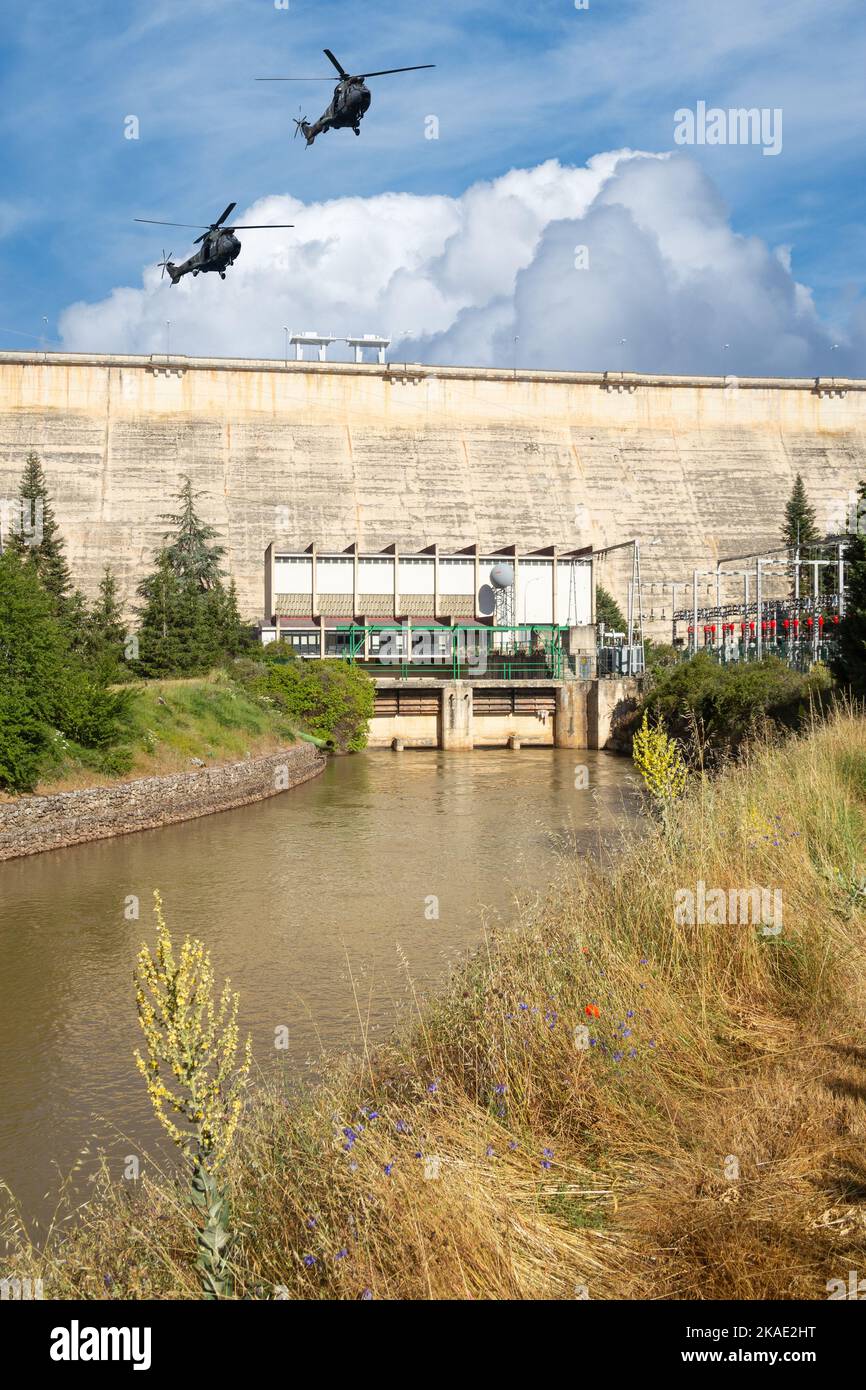 Military helicopters flying over hydro electric dam. Concept image: military attack on Ukraine power, energy infrastructure, Russia, conflict, war.. Stock Photo