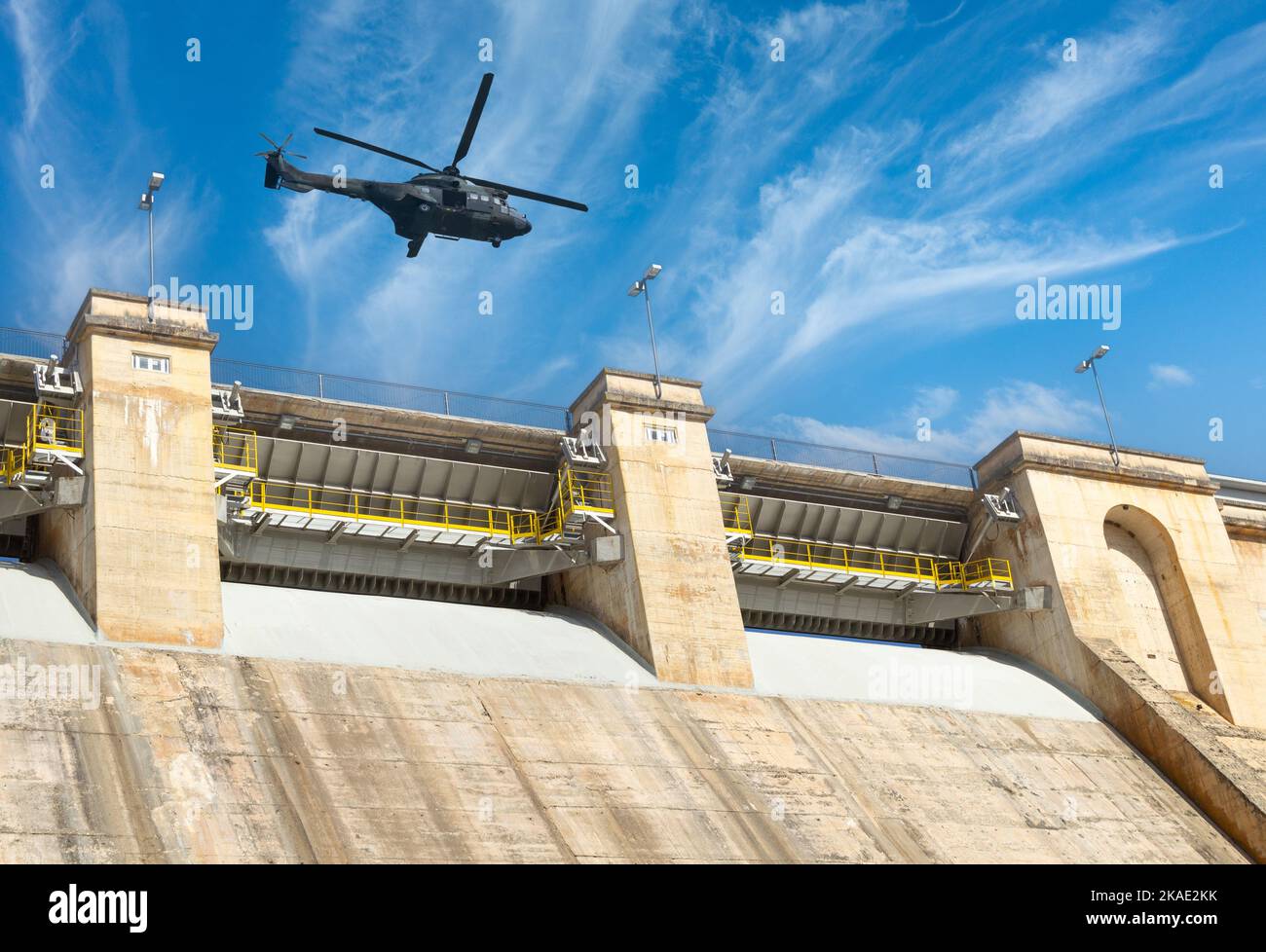 Military helicopter flying over hydro electric dam. Concept image: military attack on Ukraine power, energy infrastructure, Russia, conflict, war.. Stock Photo