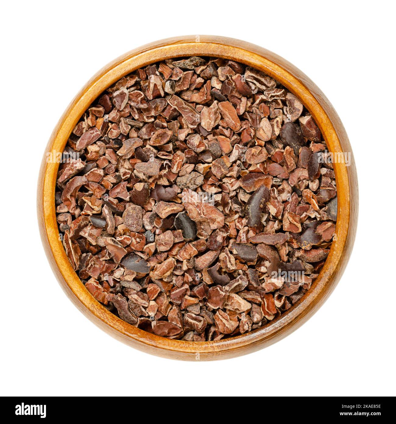 Cocoa nibs in a wooden bowl. Pieces of dried fermented kernels of cocoa beans, seeds of Theobroma cacao, generally processed into chocolate. Stock Photo