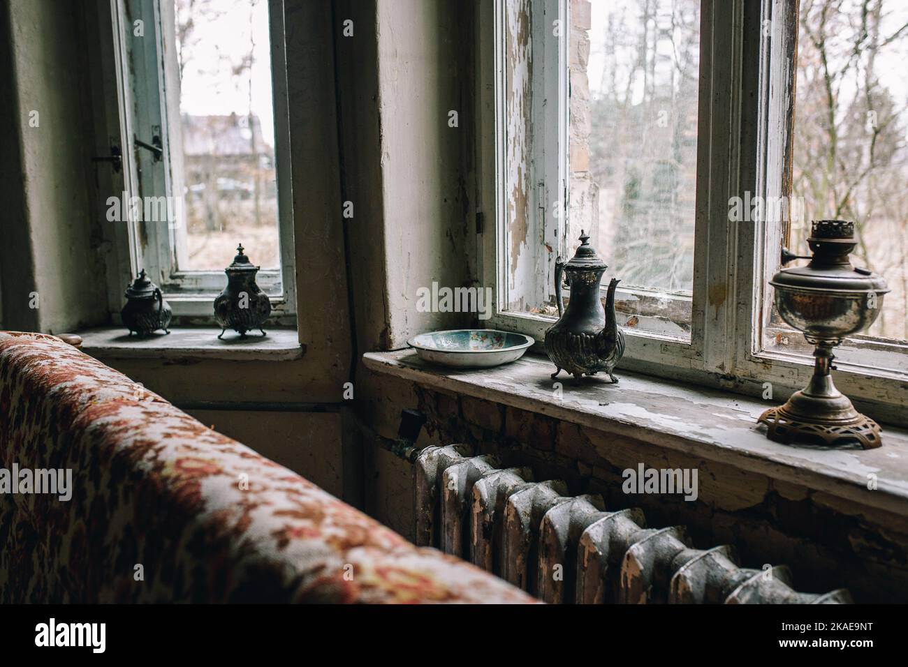 The old apartment house interior with rusty windows and antique metal teapots on the sill Stock Photo