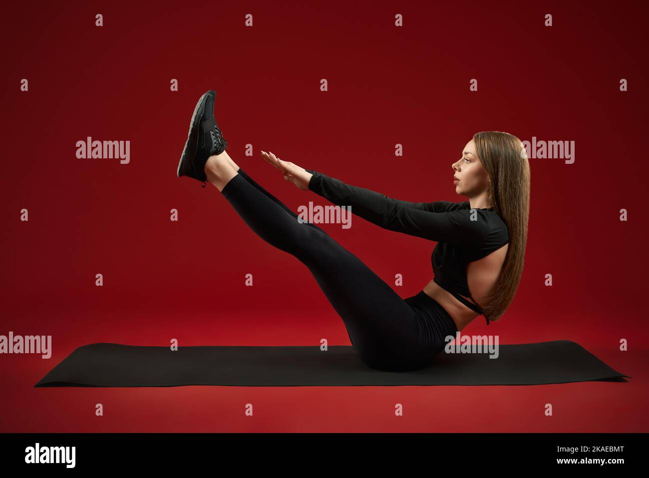 Side view of female trainer in black suite doing exercise boat pose for