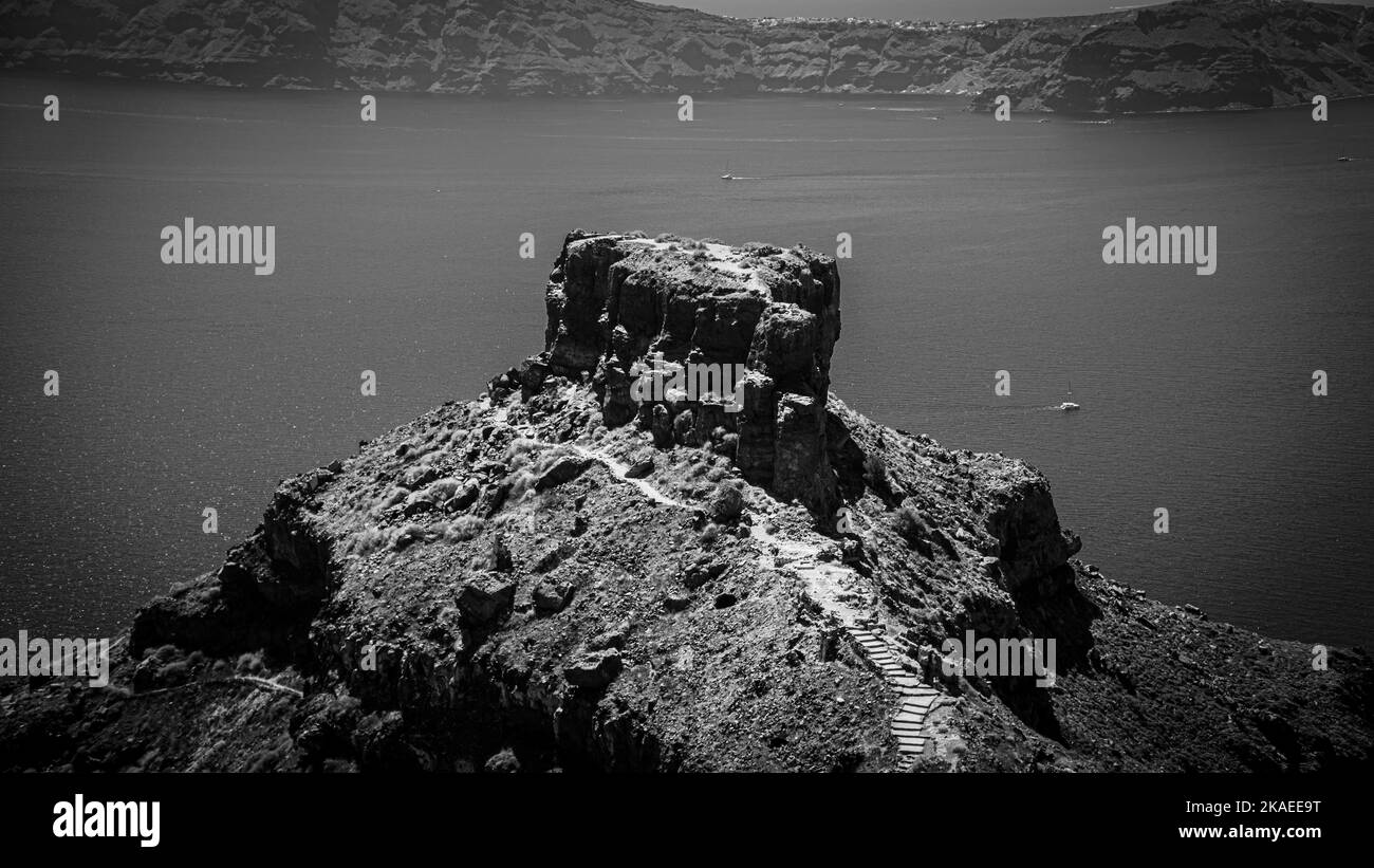 A grayscale of a rocky peak facing to the sea in Santorini, Greece Stock Photo