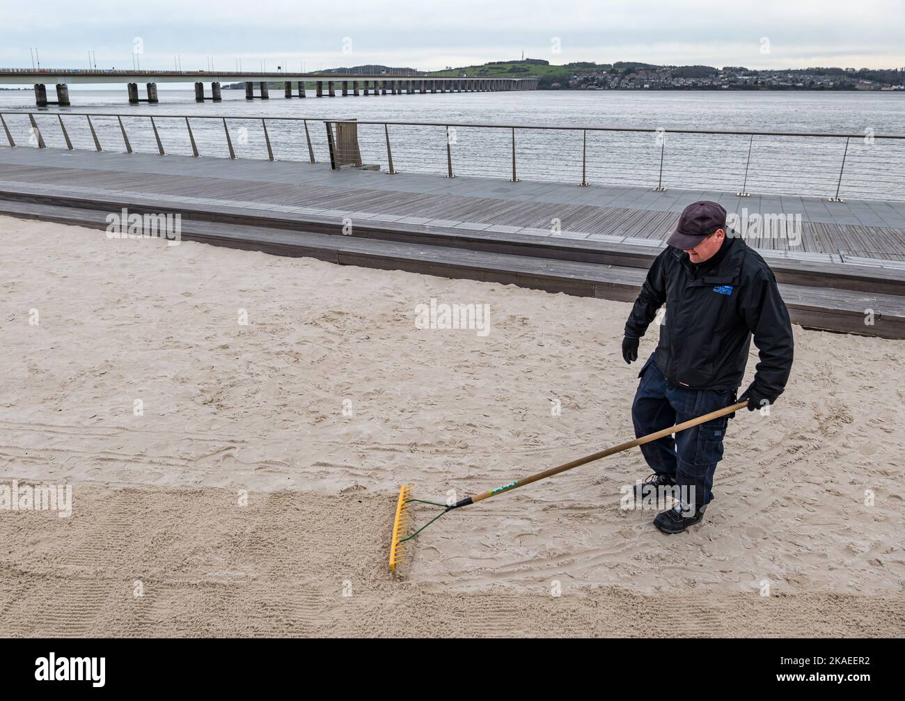 Maintenance workman raking sand on urban beach, Dundee Waterfront or Esplanade by River Tay, Scotland, UK Stock Photo