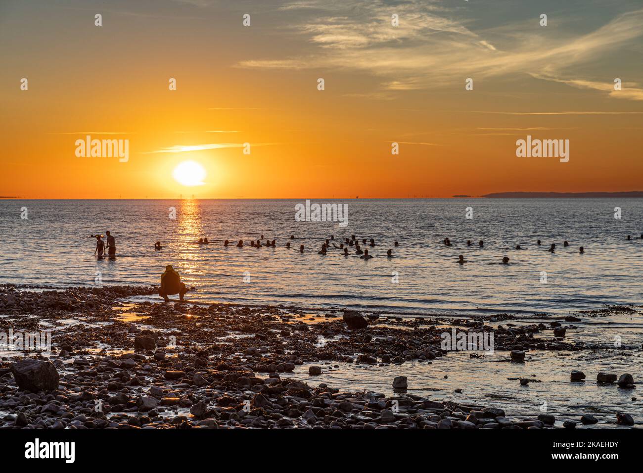 Bathers in the sea at Penarth beach at sunrise on a summers morning. Stock Photo