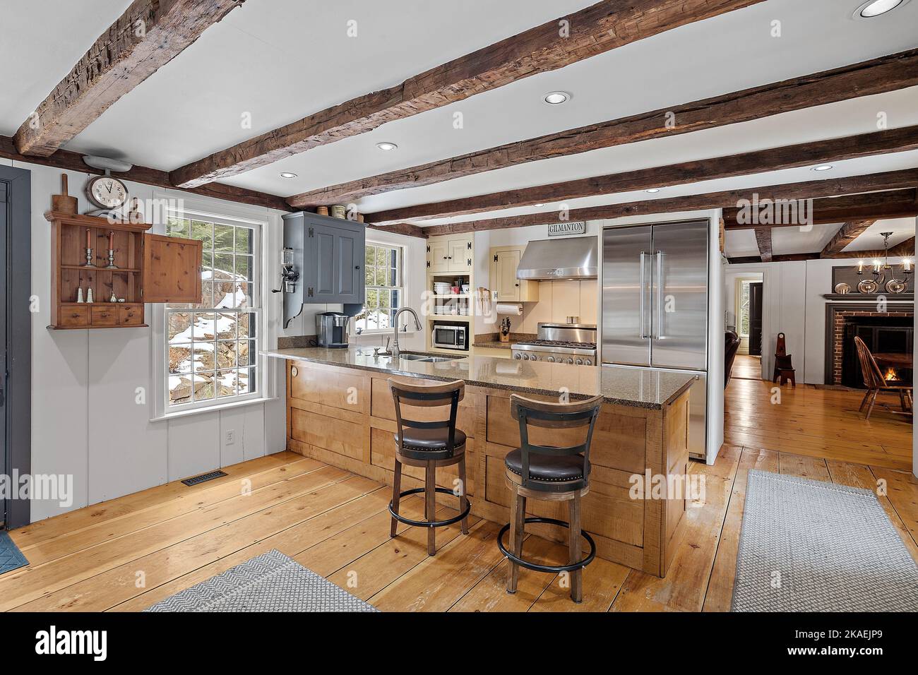 A nicely furnished bar stools and a counter with in a kitchen with brick fireplace seen behind Stock Photo