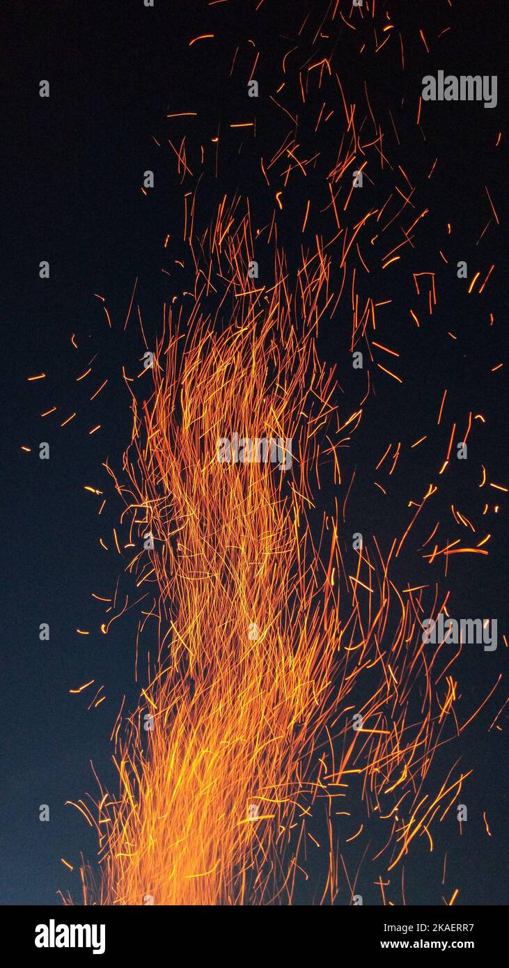 A vertical shot of flames of fire with flying burning red sparks against the dark night sky Stock Photo