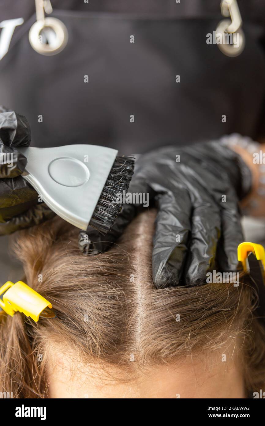 Girl in black rubber protective gloves holding a brush in her hands and stirring hair dye close-up. Colorist hair care at beauty salon hair mask. Stock Photo