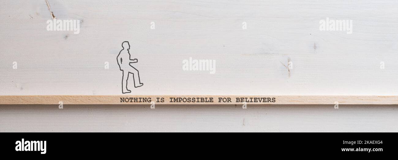 Wide view image of a silhouette of a man walking across a wooden slat with a Nothing is impossible for believers sign on it placed over plain simple w Stock Photo