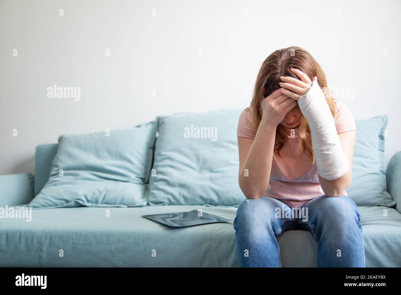 A woman with a plaster cast on her arm holds her head. Depression, despair, collapse of plans. Woman in depression. Stock Photo