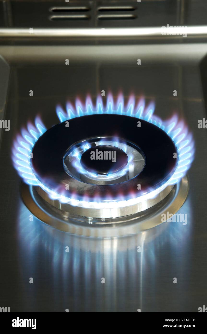 Blue flames burn from a lit gas jet on the hob of a kitchen cooker