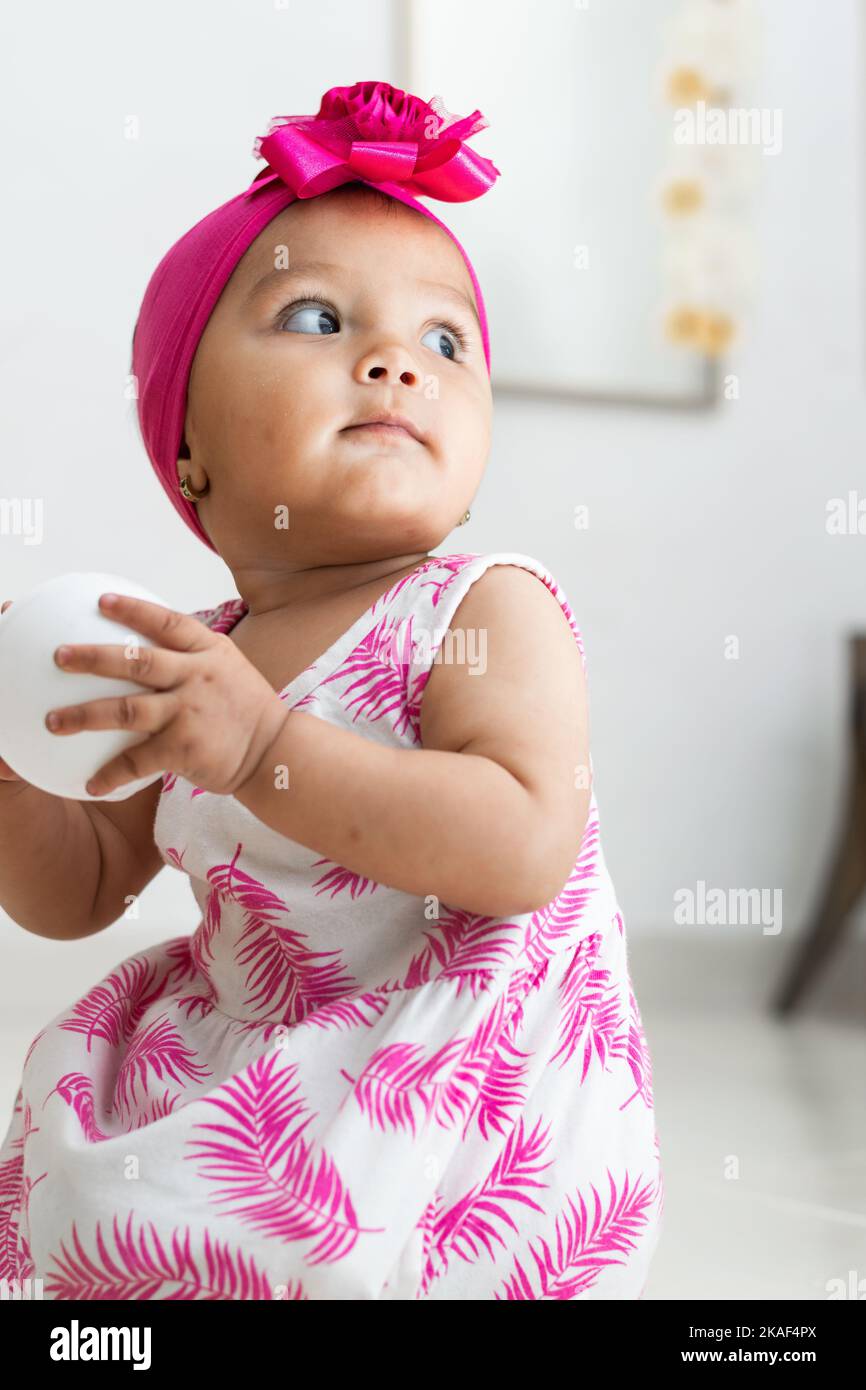 brownskinned baby girl sitting on the floor playing with a white ball