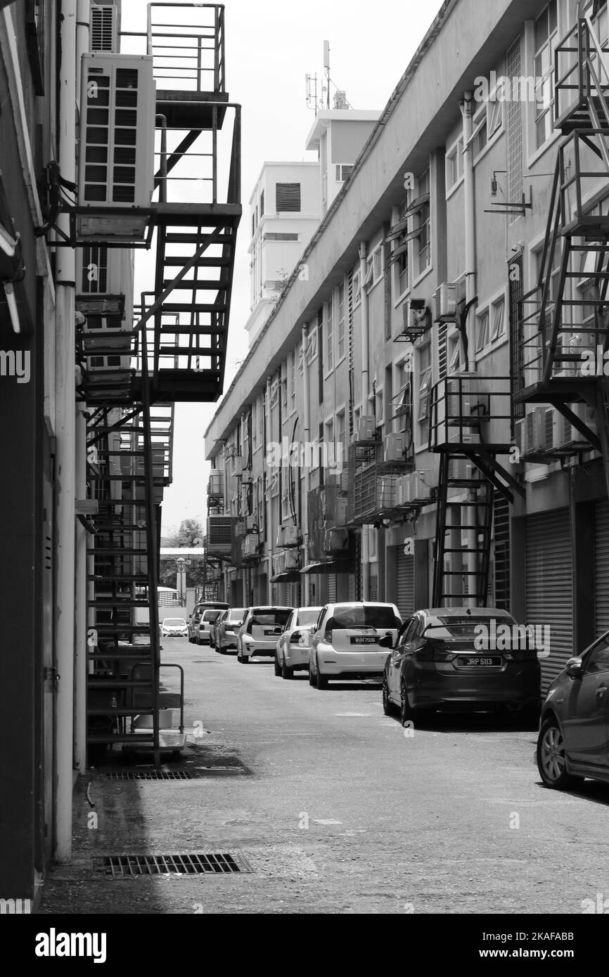 A vertical grayscale shot of cars parked along narrow alley between ...