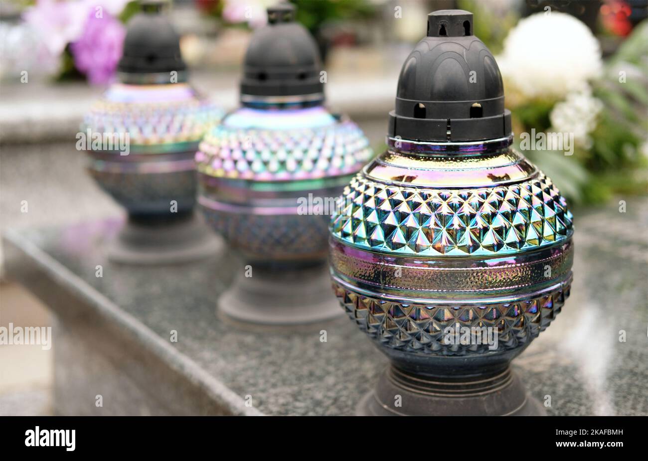 three glass candles lit on grave in memory of dead loved ones on