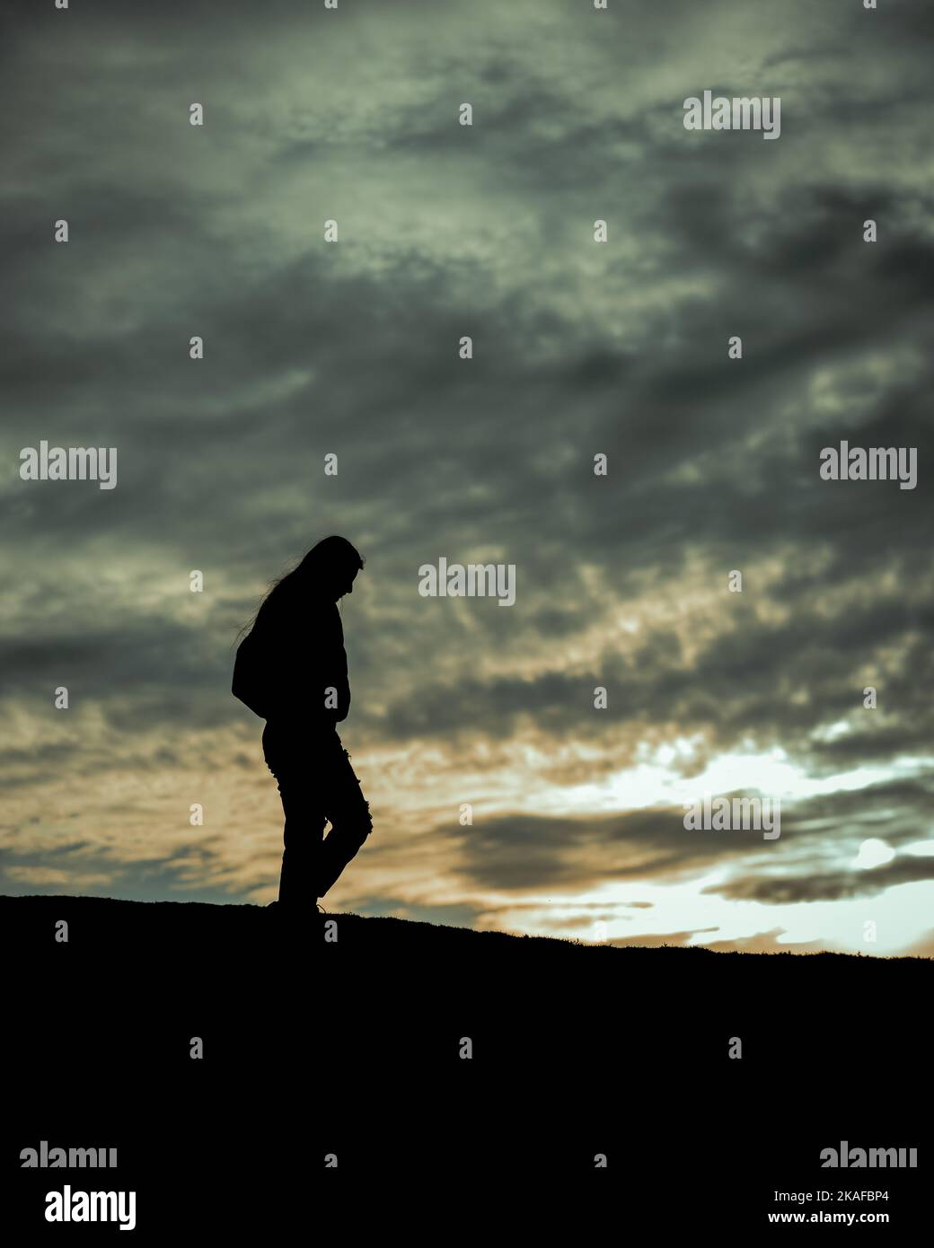 A vertical shot of a silhouette of a lonely person walking at sunset ...