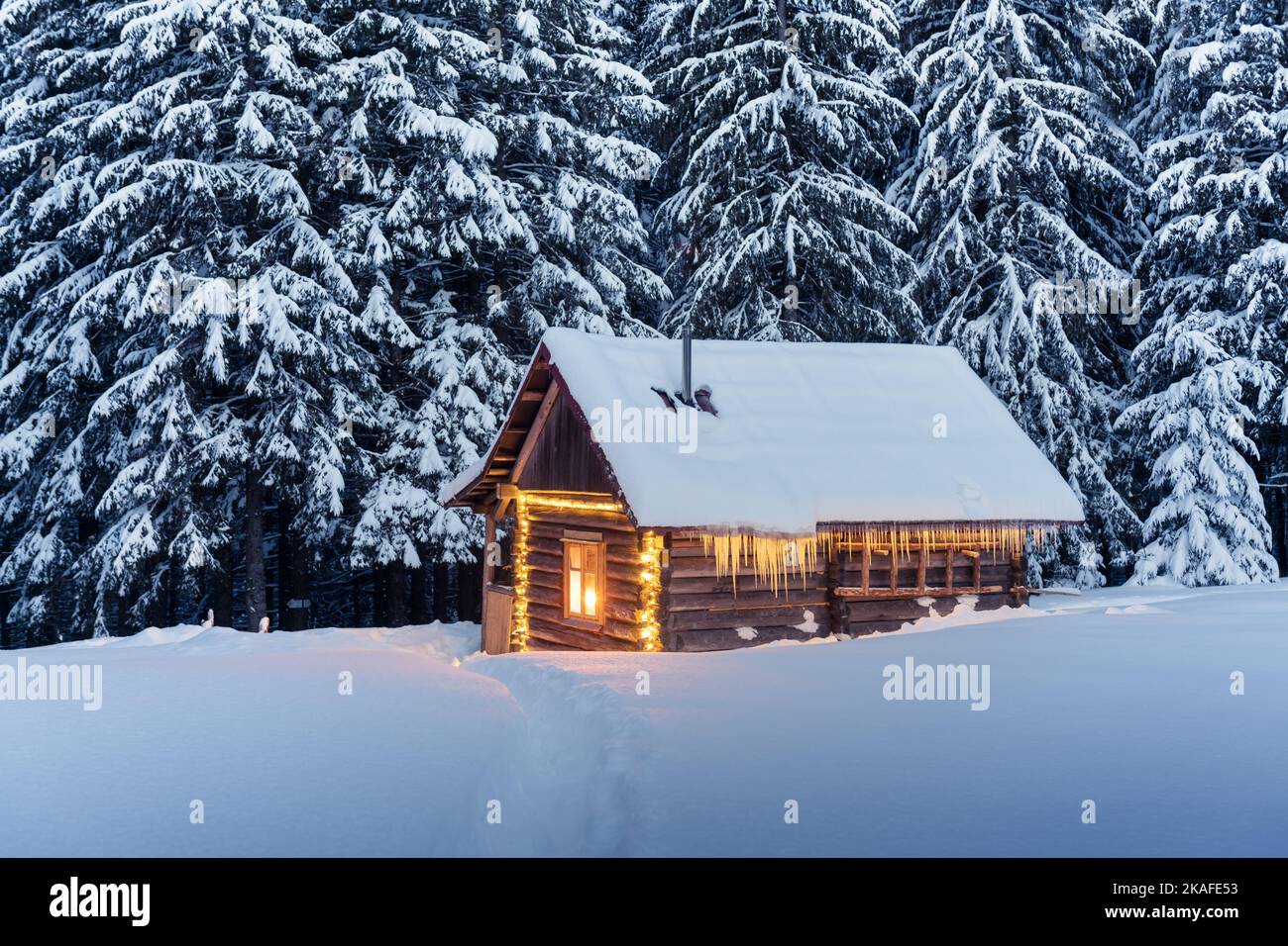 Fantastic winter landscape with glowing wooden cabin in snowy forest ...