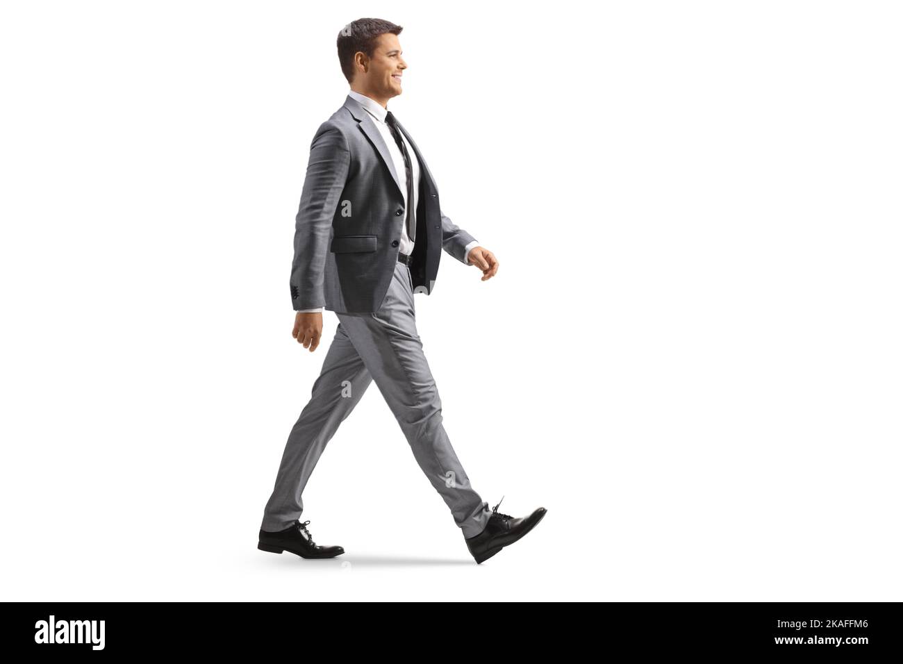 Full length profile shot of a young professional man in a gray suit walking isolated on white background Stock Photo