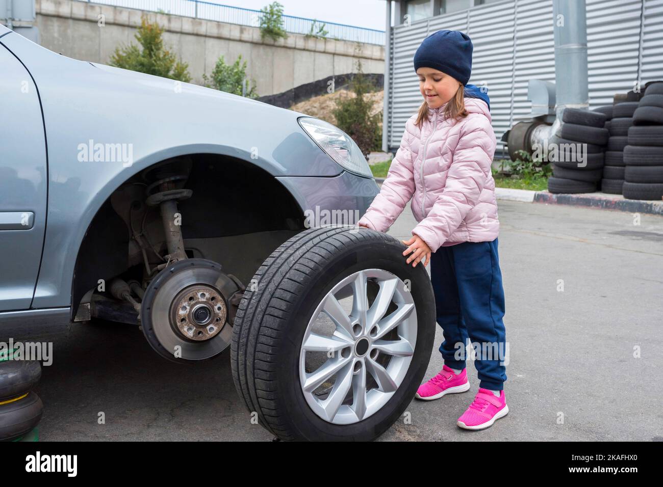 Little girl in a car service, on replacing wheel tires and servicing a