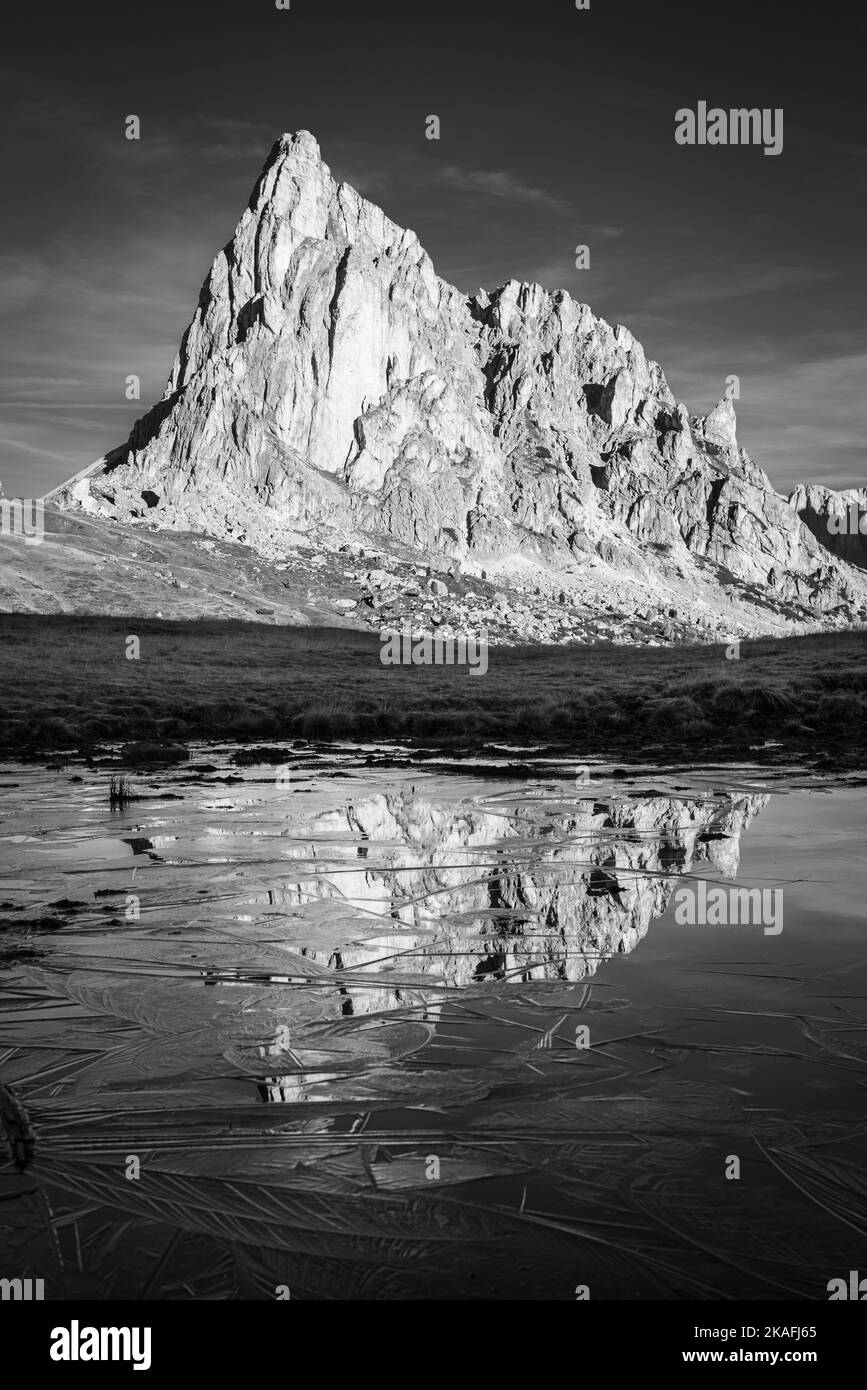 The rock face of Mount Ragusela reflected in the water and ice of a pond on a frosty autumn morning at Passo di Giau, Dolomites, Italy Stock Photo