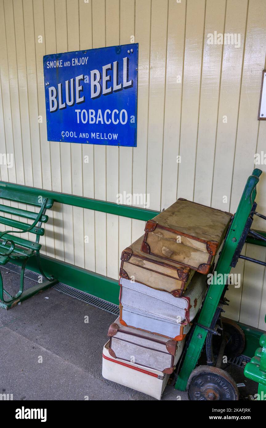 Vintage advertising sign on East Grinstead station building and porter's trolley loaded with suitcases. Bluebell Railway line, East Sussex, England. Stock Photo