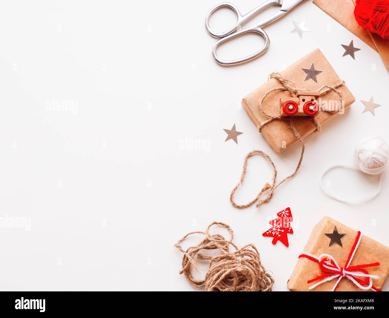 Christmas and New Year DIY presents in craft paper. Holiday gifts tied with white and red threads with toy train and Christmas tree symbol as decorati Stock Photo