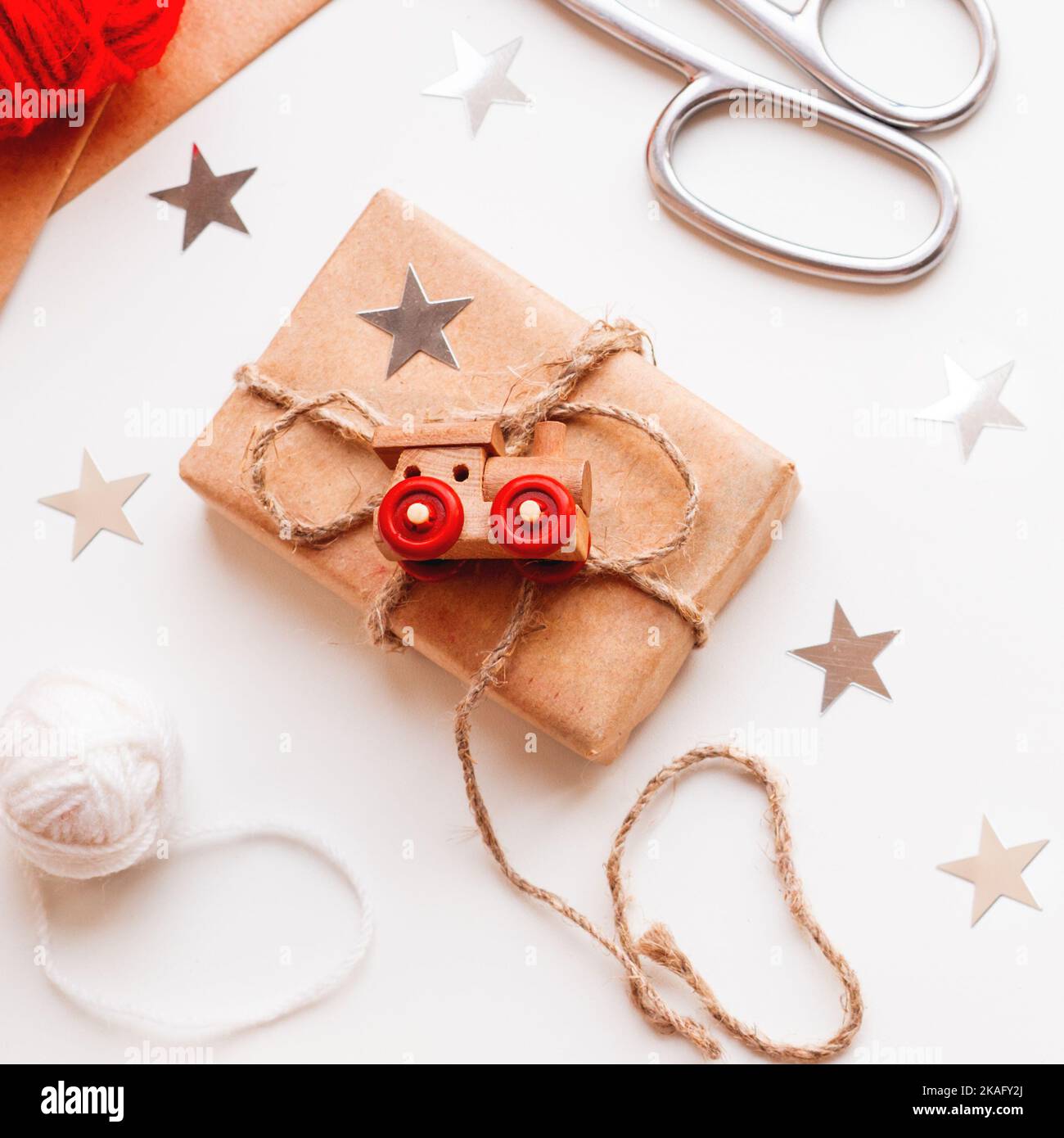 Christmas and New Year DIY presents in craft paper. Holiday gifts tied with white and red threads with toy train as decoration. Stock Photo