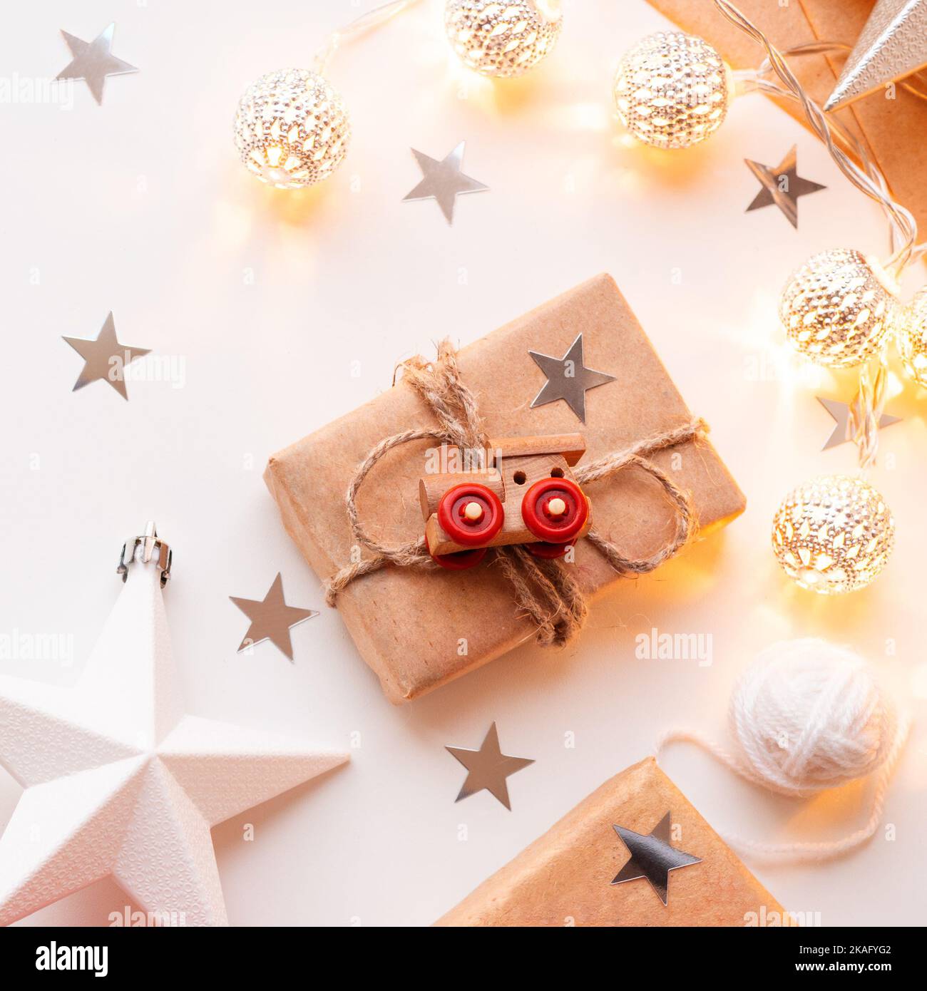Christmas and New Year wrapped DIY presents in craft paper. Gift tied with rustic thread with toy train as decoration. Metal light bulbs with delicate Stock Photo