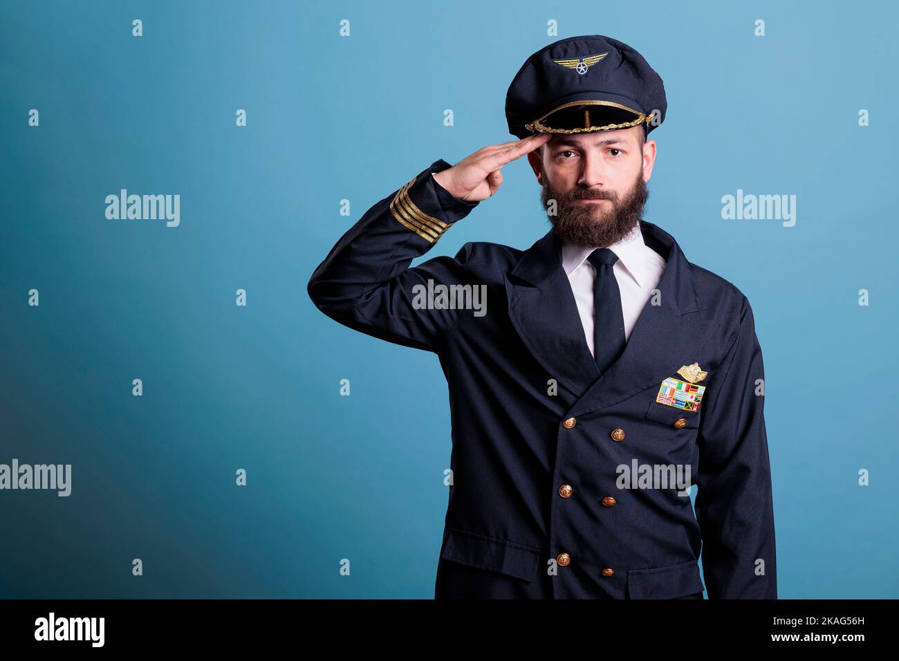 Serious airplane pilot saluting, wearing uniform and hat front view
