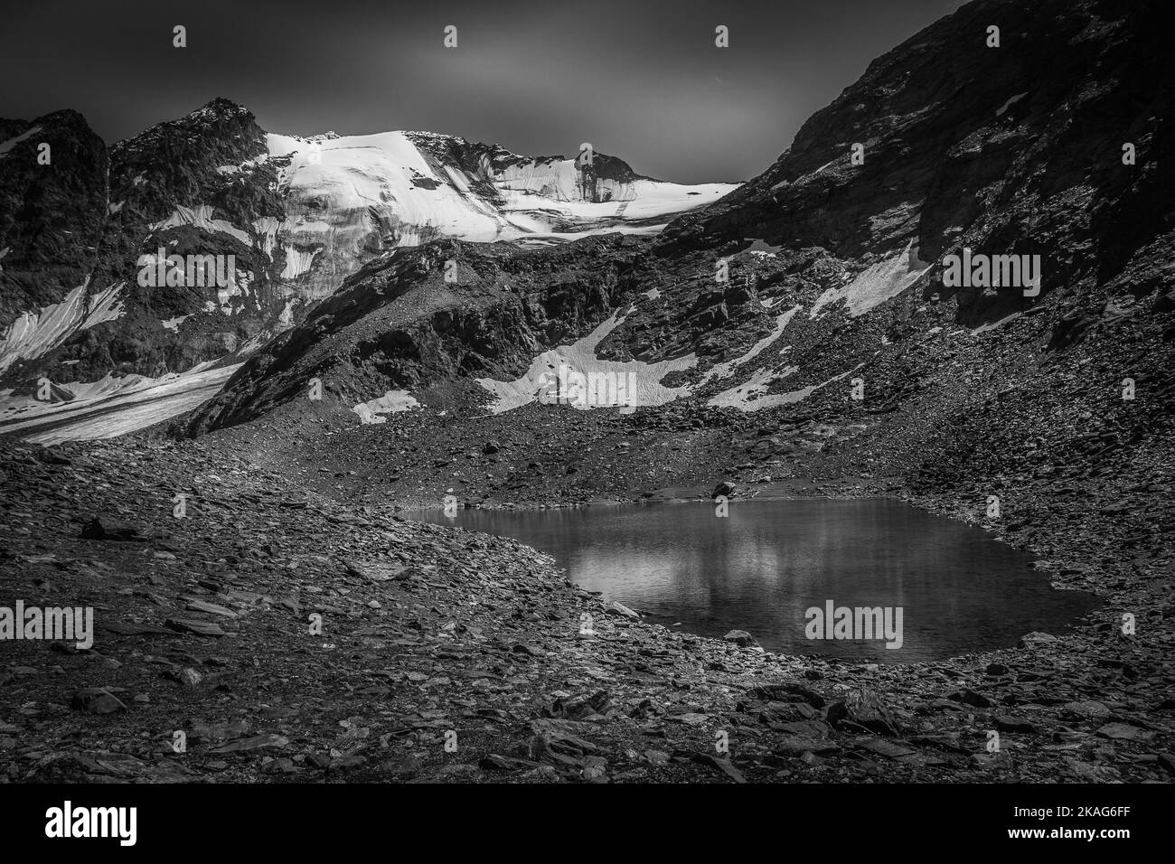 Black and white view of small green glacial lake among moraines Stock Photo