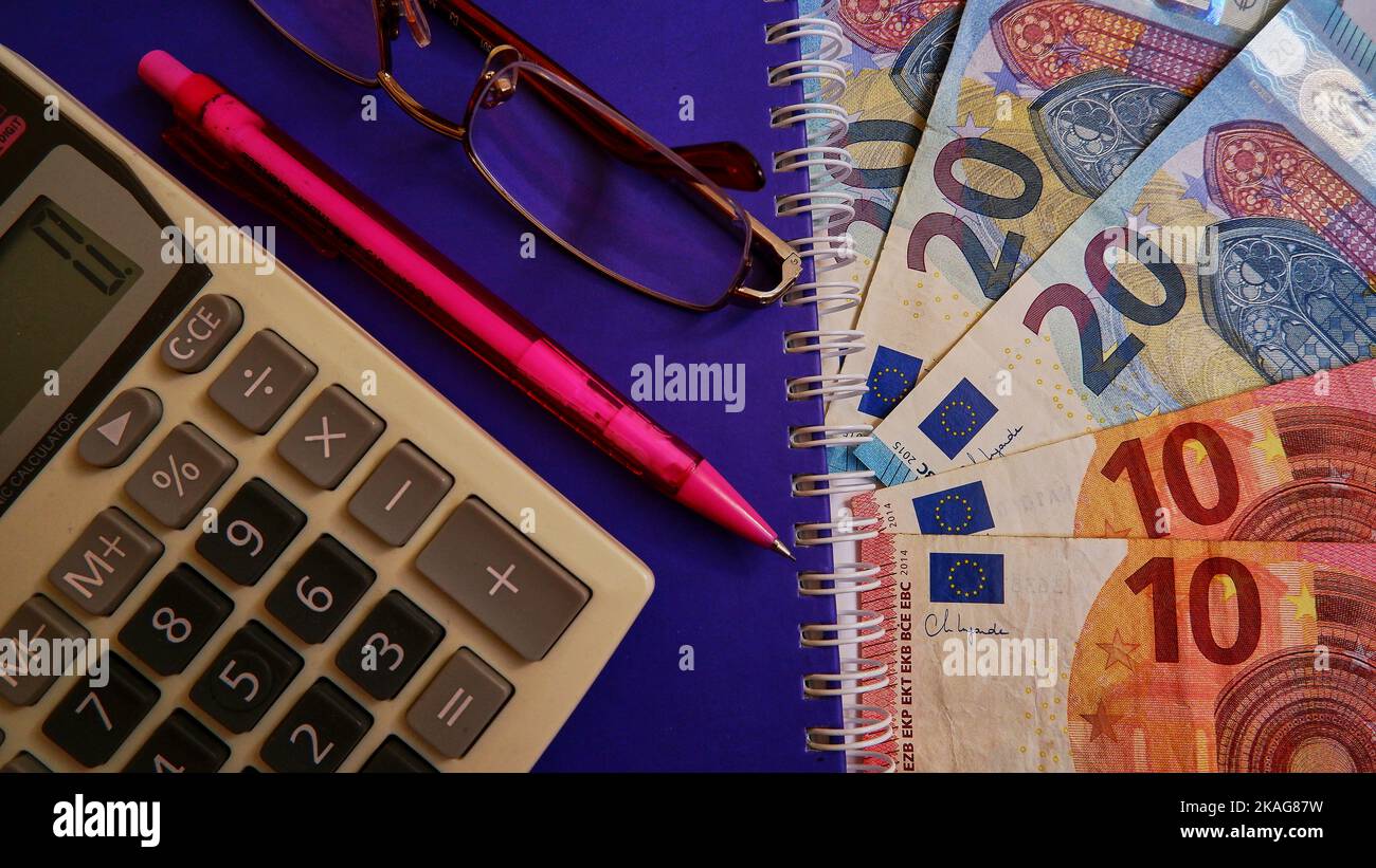 Euro money, Euro with calculator, pen or pencil and glasses on the purple notebook backgorund, top view photo. Stock Photo