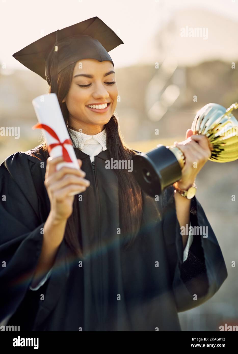 Hard work will always be rewarded. a student holding her diploma and trophy on graduation day