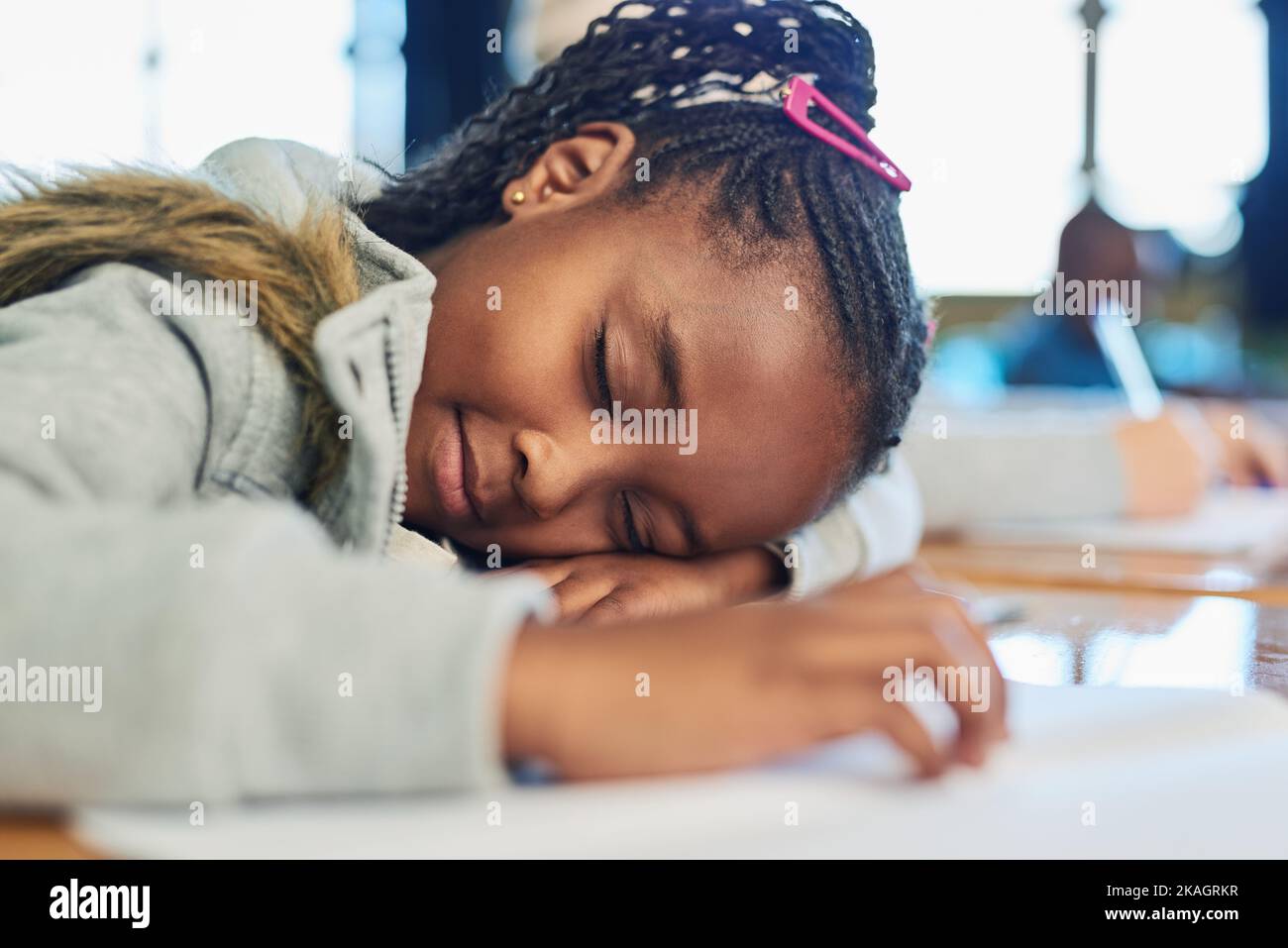 Her little brain can only carry so much. an elementary school girl sleeping on her desk in class. Stock Photo