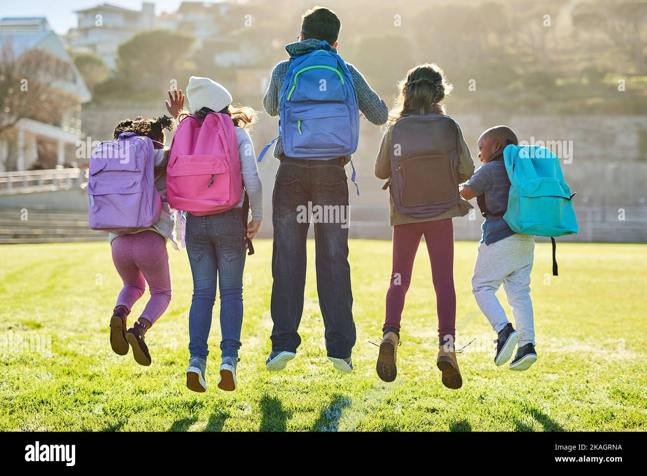 Jumping into a day of fun and learning. Rearview shot of a group of elementary school kids playing together outdoors. Stock Photo