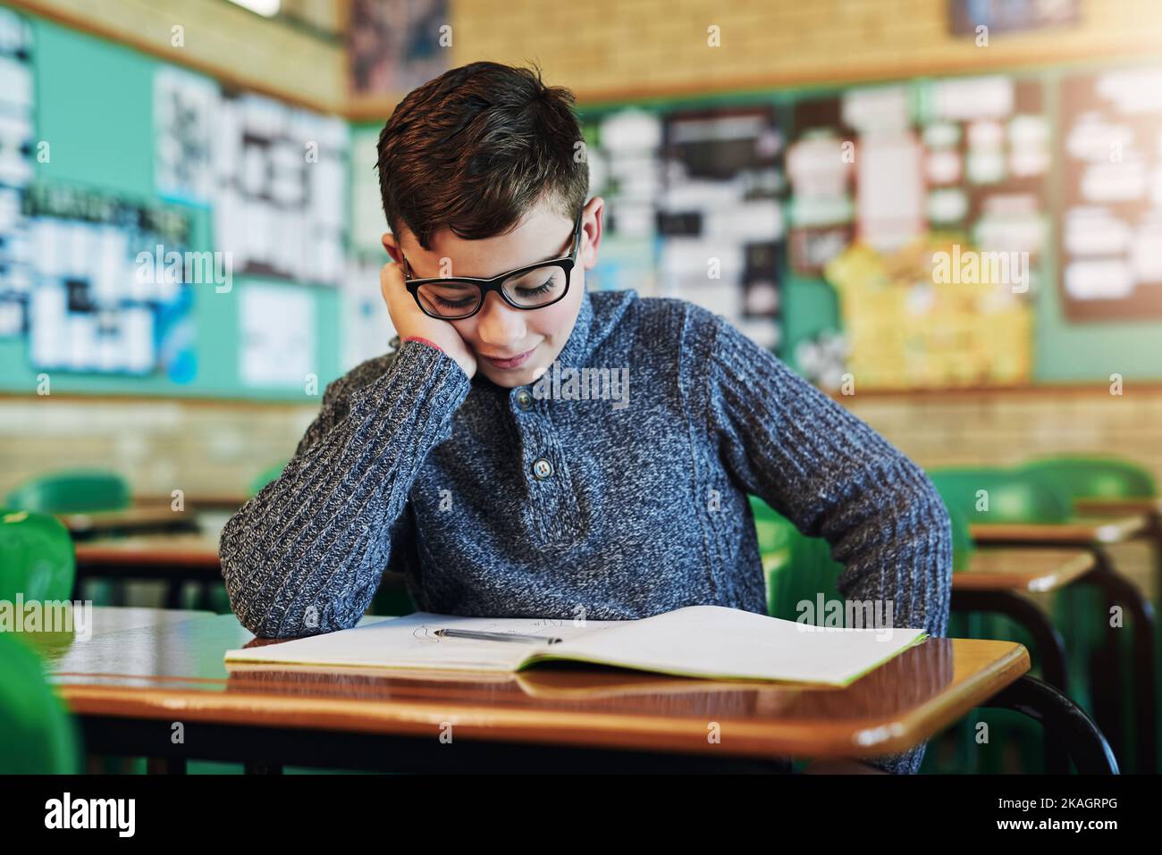 He always falls asleep when reading that book in class. an elementary school boy sleeping at his desk in class. Stock Photo