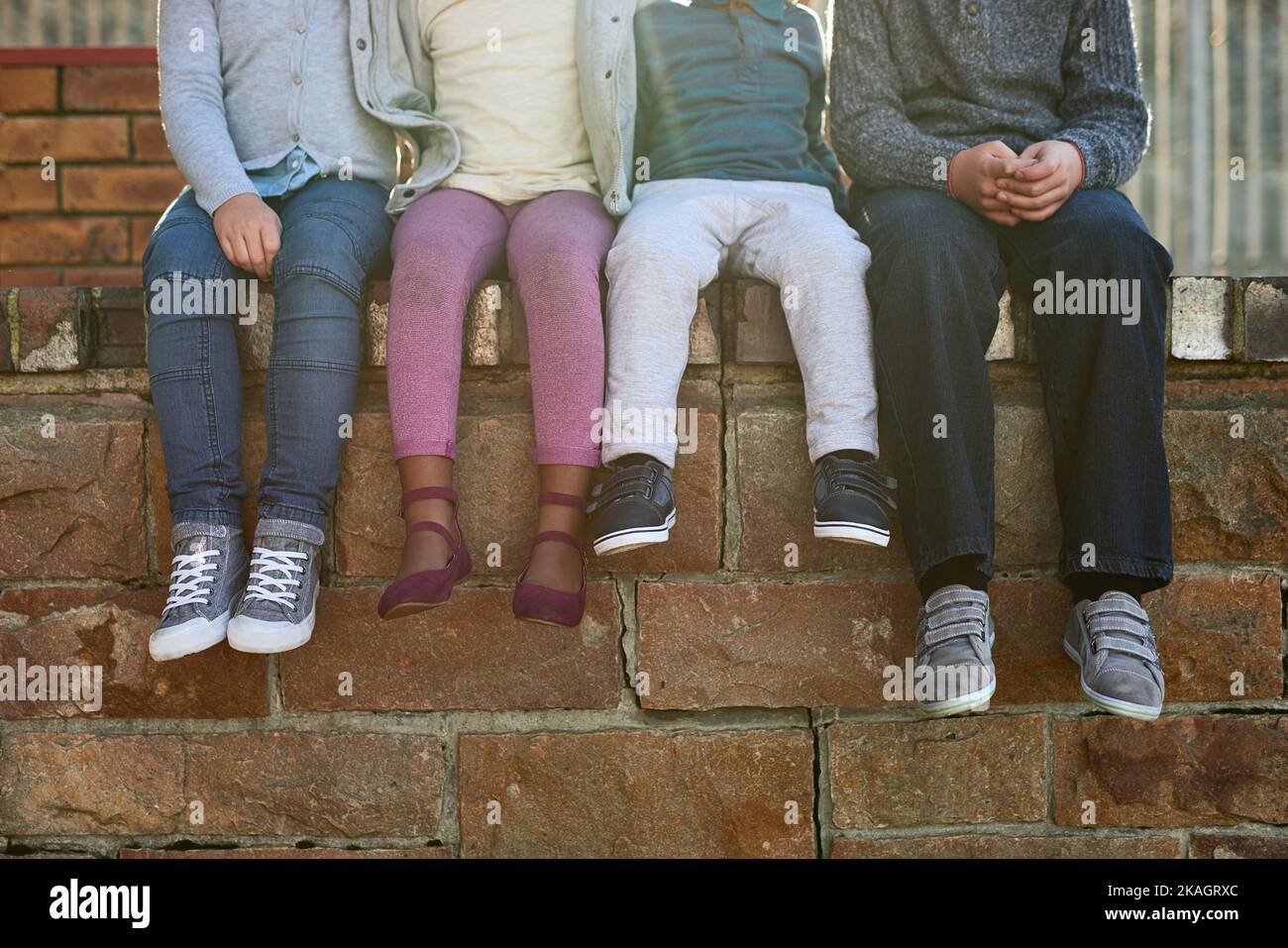 They belong to the school of cool. a group of unrecognizable elementary school kids sitting on a brick wall outside. Stock Photo