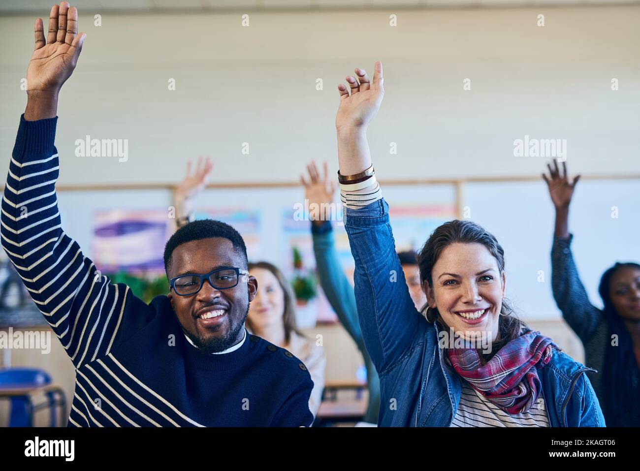 We all want more in life. a group of students raising their hands in class. Stock Photo
